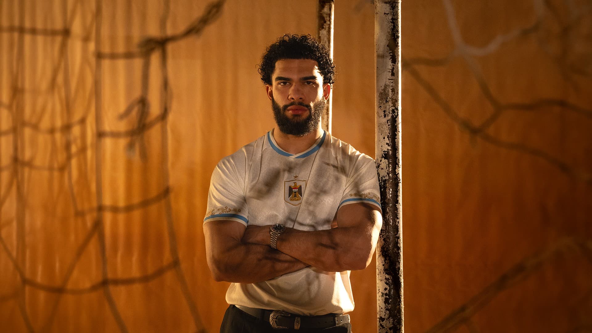 Player in a white heritage jersey, arms crossed, against a warm-toned backdrop